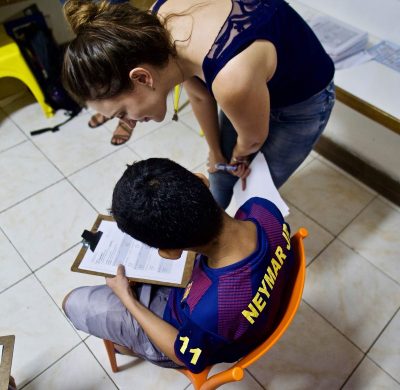 EduMais volunteer English teacher Nikola helps out a student with his work over his shoulder