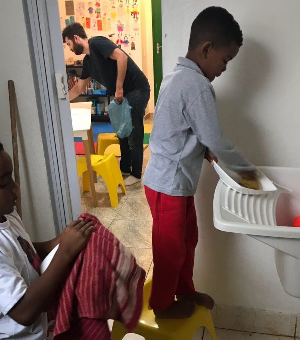 EduMais after-school students wash up their plates while volunteer Ed tidies the room in the background