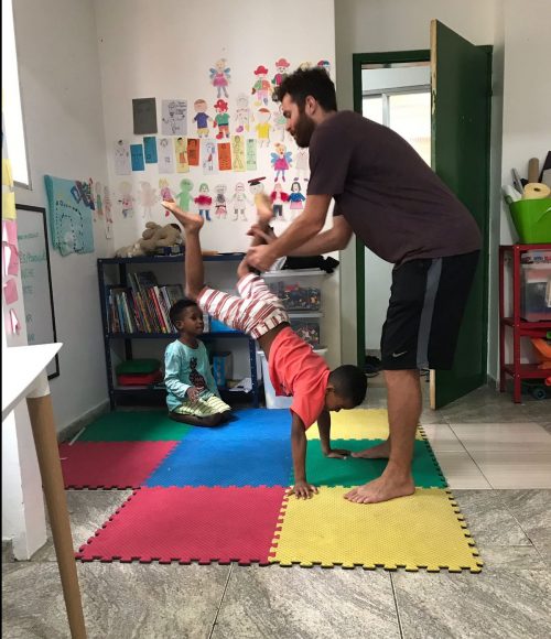 EduMais after-school program student Romulo attempts a handstand with volunteer Ed holding his legs in support