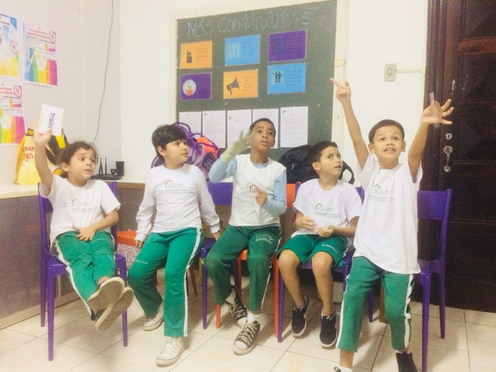 Excited EduMais English students are desperate to answer the teacher's question, with one boy even standing up from his chair in excitement