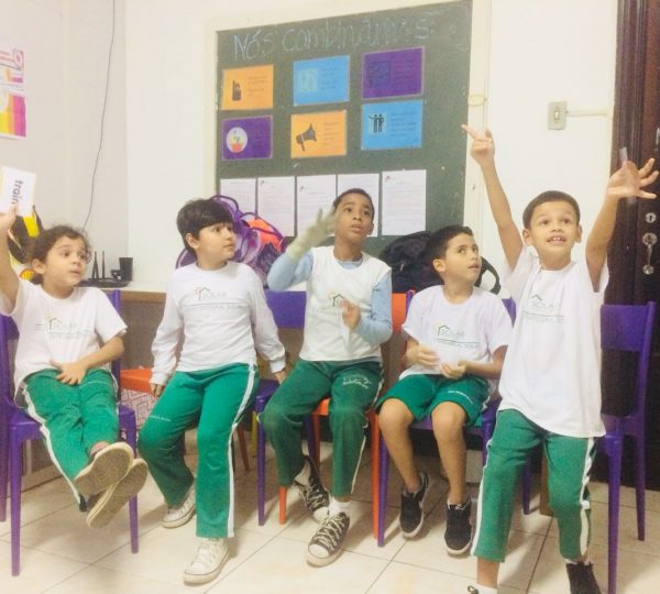 Excited EduMais English students are desperate to answer the teacher's question, with one boy even standing up from his chair in excitement