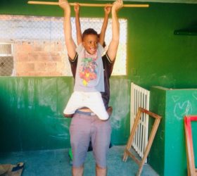 EduMais after-school volunteer Ed lifts student Renee into the air on a wooden stick