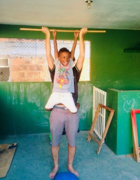 EduMais after-school volunteer Ed lifts student Renee into the air on a wooden stick