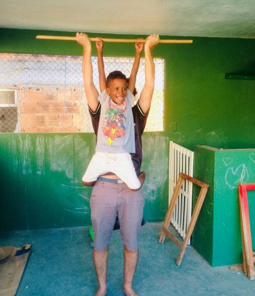 EduMais after-school volunteer Ed lifts student Renee into the air on a wooden stick