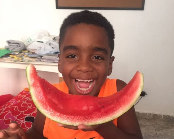 EduMais after-school program student Andre grins widely with an eaten segment of a watermelon