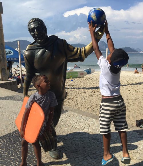 One of EduMais's after-school boys jumps to put a football in the hand of the Dorival Caymmi statue on Copacabana Beach, Rio de Janeiro