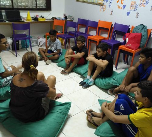 EduMais Programming Camp students sit on green cushions with their volunteer teacher Roger and EduMais founder Diana NIjboer