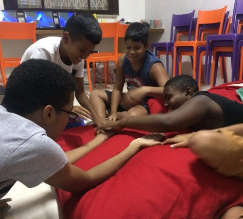 Boys at EduMais's Programming Camp 2019 sit in a circle and stretch out all their hands to touch in the middle with their volunteer teacher Roger