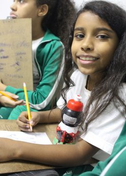 EduMais student smiles for the camera while working with a pencil and paper on her English skills