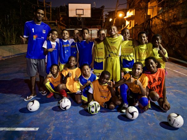 EduMais football program leader William with 15 of his students on the pitch at night and five soccer balls