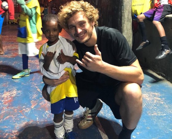 EduMais football volunteer Mads poses with the program's youngest student, who is about a third of his size