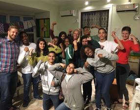 EduMais students and volunteer teachers in the classroom with many striking a pose by curling their biceps