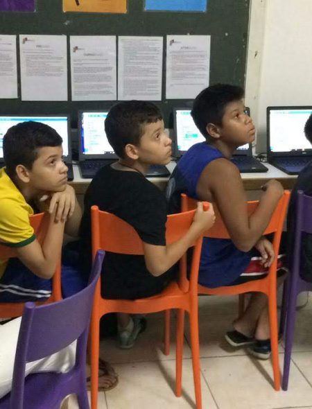 Four boys on EduMais's Programming Camp look intently at the whiteboard in the EduMais classroom in front of their computers and with volunteer Audrey