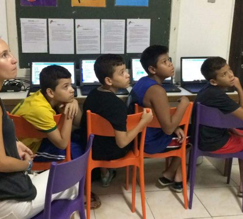 Four boys on EduMais's Programming Camp look intently at the whiteboard in the EduMais classroom in front of their computers and with volunteer Audrey